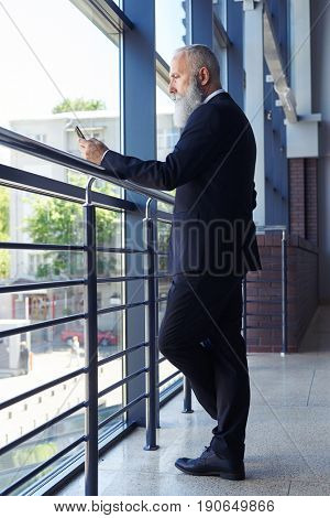 Vertical of humorless male with gray beard surfing in phone