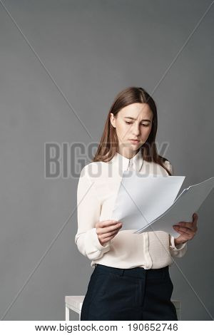 Businesswoman holds the papers in her hands and reads what is written there. Isolated on gray background