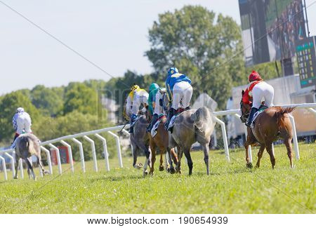 STOCKHOLM SWEDEN - JUNE 06 2017: Rear view of standing colorful jockeys on gallop race horses riding in a curve at Nationaldags Galoppen at Gardet. June 6 2017 in Stockholm Sweden