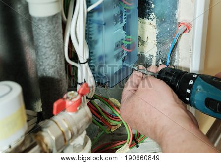 Electrician's hands are inserting wires in a switch for thermostats and servo drives valves in a home heating system.