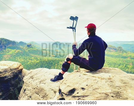 Tired Hurt Tourist With Medicine Crutches. Man With  Broken Leg In Knee Brace Features Resting On  E