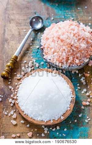 Different types of natural salt in stone bowls on wooden surface. White sea salt pink Himalayan salt
