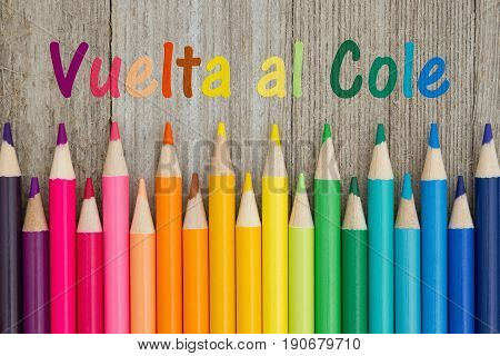 Back to School in Spanish Vuelta al Cole text with colorful pencil crayons on a weathered wood