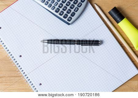 Work desk with note pad calculator and biro on wooden table from above