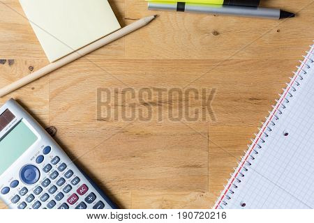 Work desk with note pad calculator and biro on wooden table from above