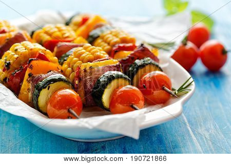 Grilled vegetarian skewers with zucchini, onion, bell pepper, corn and cherry tomatoes in a herb marinade on white plate