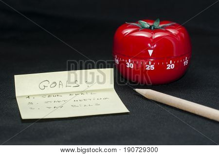 Mechanical Tomato shaped kitchen timer for cooking studying and working with pencil and goal list.