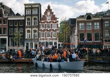 Amsterdam Netherlands - 25 April 2017: Local people and tourists dressed in orange clothes ride on boats and participate in celebrating King's Day along the canal and promenade of Amsterdam.