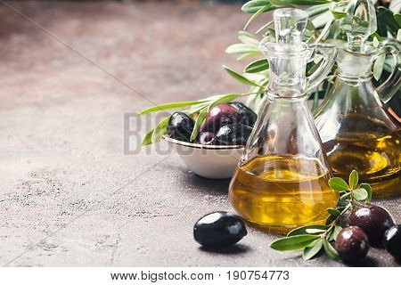 Olive oil in a glass bottle and olive branch on brown stone table