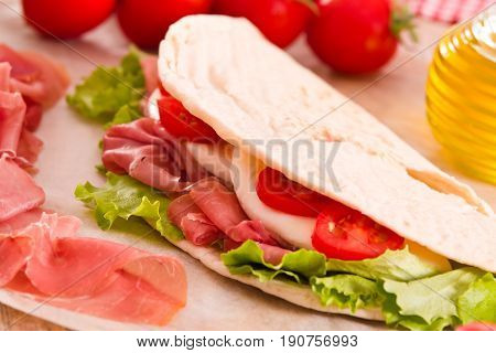 Piadina with ham and lettuce on wooden table.