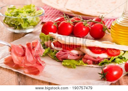 Piadina with ham and lettuce on wooden table.