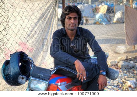 Bandar Abbas Hormozgan Province Iran - 16 april 2017: A portrait of an Afghan man who is resting in the shadows sitting on the saddle of his motorcycle.