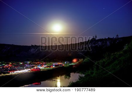 Wonderful landscape with rocks and mountains at orheiul vechi memorial in moldova, night view with full moon and reflection in the raut river and monastery with church and cars