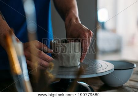 Close up of male hands working with clay on artisan working stand from dry wood surrounded by artistic workshop tools and implements creates poterry diy