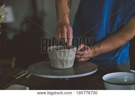 Close up of male hands working with clay on artisan working stand from dry wood surrounded by artistic workshop tools and implements creates poterry diy