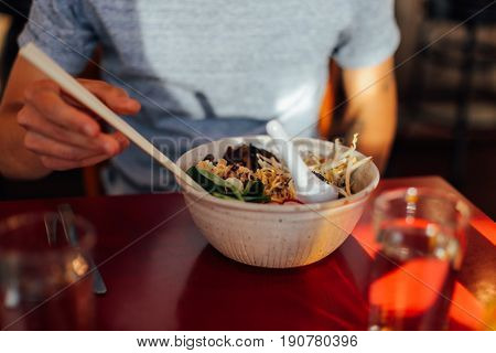 Soft focused shot of vegeterian vegan asian fusion dish with authentic natural ingridients in fancy downtown cafe restaurant hipster man eating with chopsticks