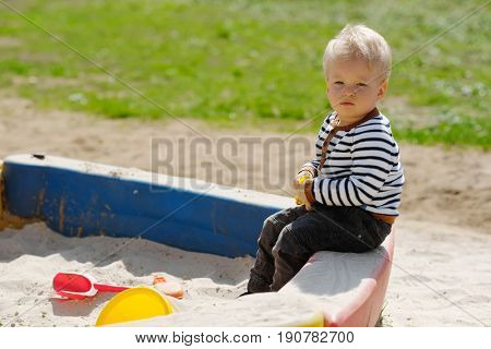 Portrait of toddler child outdoors. One year old baby boy playing with sand at playground sandbox