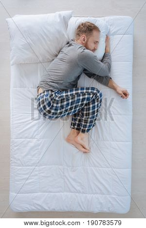Feeling comfortable. Nice handsome pleasant man lying comfortably on the bed and enjoying his relaxation while being at home
