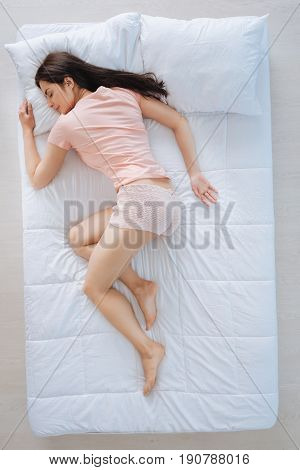 Enjoyable relaxation. Pleasant peaceful cute woman resting in her bed and enjoying her relaxation while being at home