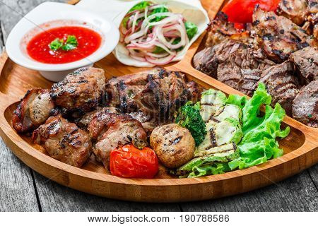 Assorted delicious grilled meat and vegetables with fresh salad and bbq sauce on cutting board on wooden background close up. Hot Meat Dishes. Top view