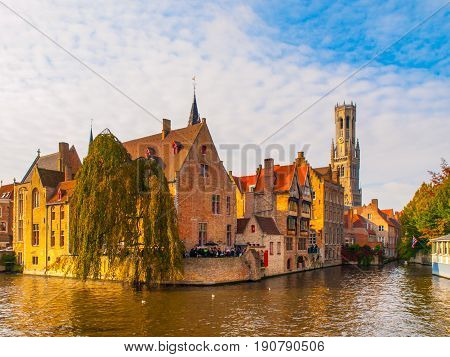 Cityscape of Bruges, Flanders, Belgium. Water canal at Rozenhoedkaai with old brick buildings and Belfry Tower on background.