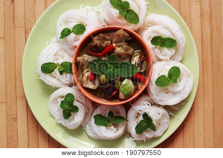 Green curry in an orange cup in the middle of a plate Thai-rice-flour Noodles (kanom jeen)