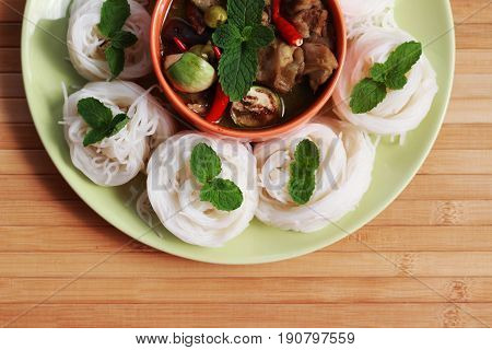 Green curry in an orange cup in the middle of a plate Thai-rice-flour Noodles (kanom jeen)