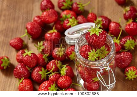 Fresh red strawberries for jam in a glass jar on the brown wooden table. Many strawberries in the glass jar and on the table. Horizontal photo. Seasonal fruits. Food backgrounds and still-life. Concept of the vitamin food.
