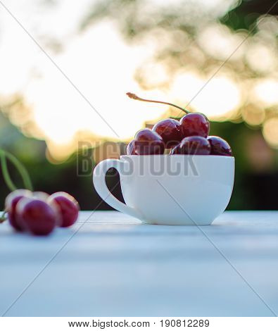 Sweet cherries in a cup on a wooden table and sun rays