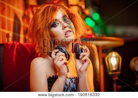 Redhaired girl in headphones with unusual makeup at the disco