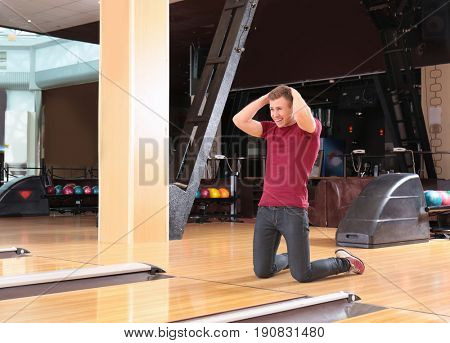 Upset young man standing on knees in bowling club