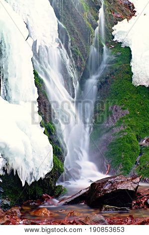 Winter View To Cascade Of Waterfall, Icy Snow On The Rocky Wall And Boulders In Rapid Stream. Reflec