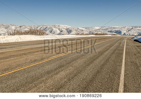 Paved plowed and dry road in Utah with snow in the mountains and a clear blue sky