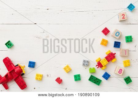 Top view on wooden cubes with numbers and colorful toy bricks and plane on white wooden background. Toys in the table