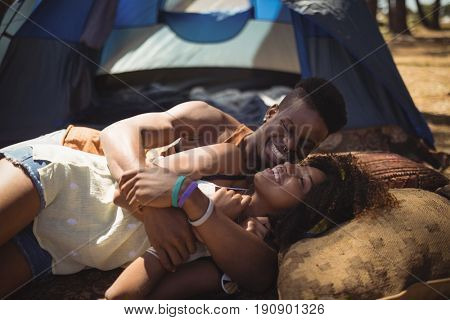 Close of happy couple lying on field against tent at forest