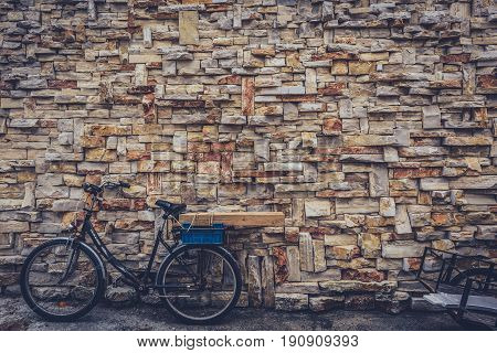 Old rusty vintage bicycle bike and decorative stone wall. Street photo of old bike and trolley leaned against a stone wall on a street of Silba Croatia.