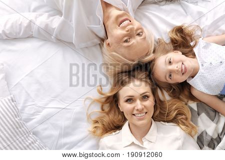 No generation gap. The top view of three happy cheerful faces of three females of different ages lying head to head and enjoying themselves together