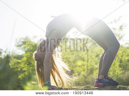 Young woman in gray top practicing yoga in beautiful nature. Stretch workout outdoor evening