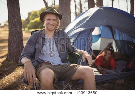 Portrait of smling man sitting on chair by tent at forest
