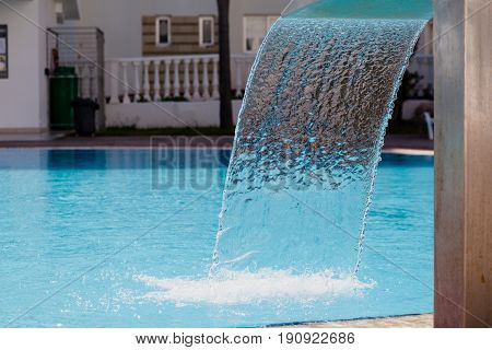 Waterfall jet and texture of falling water at the background of turquoise water in the swimming pool