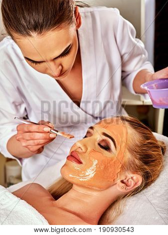 Collagen face mask. Facial skin treatment. Woman receiving cosmetic procedure in beauty salon. Bottle with moisturizing cream on background. Mask against black dots.