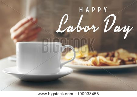 Cup of coffee and breakfast on table. Text HAPPY LABOR DAY on blurred background