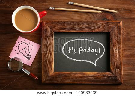 Small chalkboard with text IT'S FRIDAY and cup of coffee on wooden background
