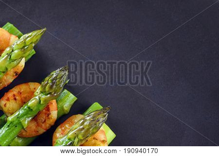 green asparagus with tiger prawn shrimp on a dark gray plate top view from above with large copy space festive appetizer or buffet snack