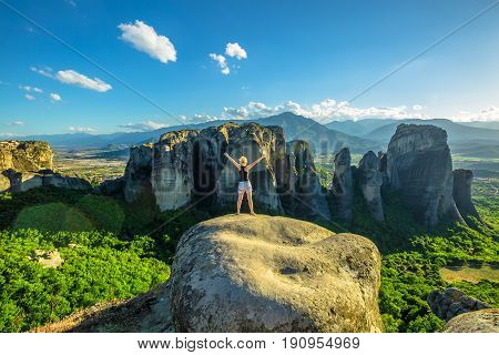 Woman traveler enjoying spectacular Meteora landscape in Thessaly, Greece. Happy female hiker freedom with arms raised outdoors. Panoramic view from best view point Psaropetra. Tourism in Europe.