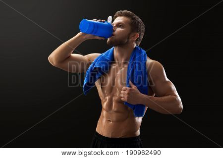 Young muscular shirtless sportsman drinking after workout posing on black background with copyspace.