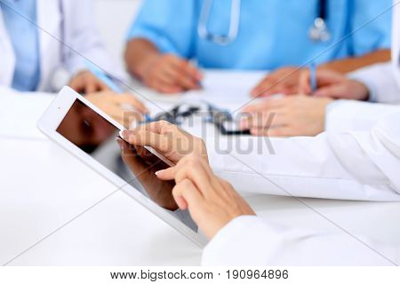 Group of doctors at medical meeting. Close up of physician using tablet computer