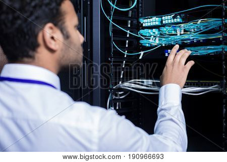 Network connection. Professional male IT administrator standing in front of the network server and checking the internet cables while doing his job
