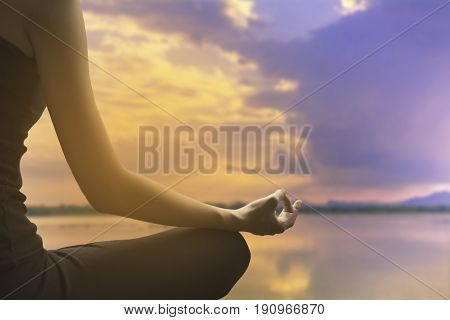 Close-up of feminine and masculine arms and crossed legs during meditation on river with sky background.