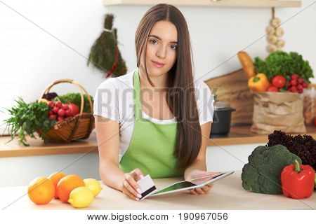 Young woman is making online shopping by tablet computer and credit card. Housewife found new recipe for cooking in a kitchen.